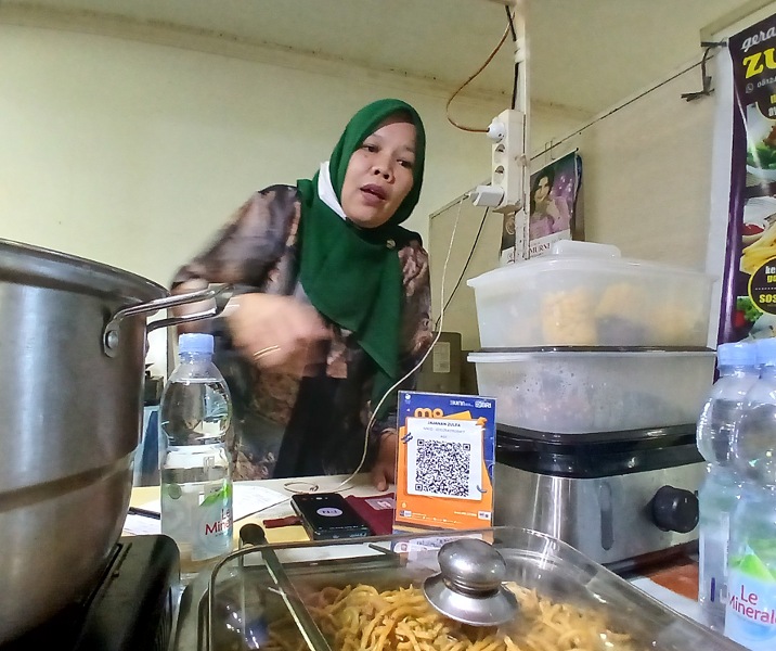 Zulfah menunjukkan QRIS BRI dan aneka makanan yang dijualnya di Kantin DWP Gedung Utama Kompleks Perkantoran Wali Kota Pekanbaru di Kecamatan Tenayan Raya. Foto: Surya/Riau1.